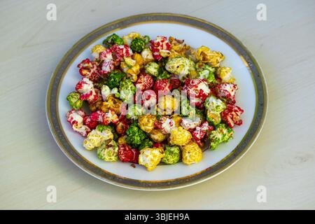 Delicious colorful sweet popcorn on a white plate, wooden background. Tasty snack. Stock Photo