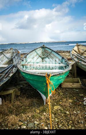Timeworn Shetland model boats decay by the shore—weathered relics of island craftsmanship slowly returning to the sea. Stock Photo
