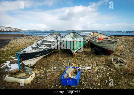 Timeworn Shetland model boats decay by the shore—weathered relics of island craftsmanship slowly returning to the sea. Stock Photo
