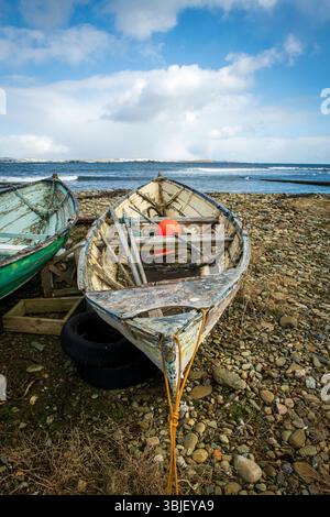 Timeworn Shetland model boats decay by the shore—weathered relics of island craftsmanship slowly returning to the sea. Stock Photo
