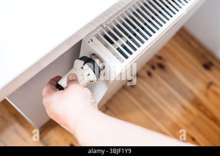 Hand regulates the heat in the house on the radiator handle. Stock Photo