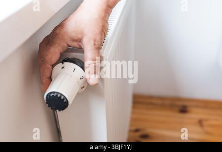 Hand regulates the heat in the house on the radiator handle. Stock Photo