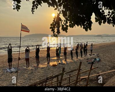 A group of people during an outside yoga class at sunset on the beach of Au Nang / Krabi (Thailand) Stock Photo