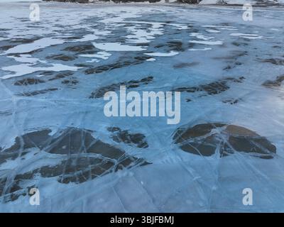 Close up aerial view of a frozen lake surface, revealing intricate patterns of cracked ice and exposed darker patches Stock Photo