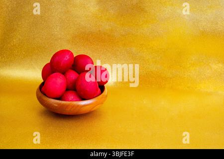 Red boiled easter eggs pile in a wooden bowl on golden glitter background Stock Photo