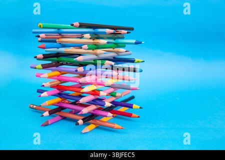 Stacked colored crayons stacked in the shape of a high tower illuminated  on blue Stock Photo