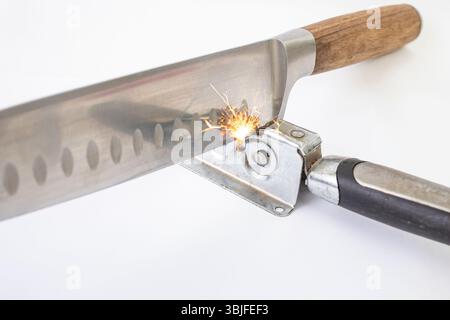 Vintage knife sharpener with a santoku chef knife, and orange sparks isolated on white Stock Photo