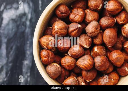 Hazelnuts in ceramic bowl. Brown healthy snack. Organic vegan nuts. Closeup of shelled texture. Rustic marble background. Stock Photo
