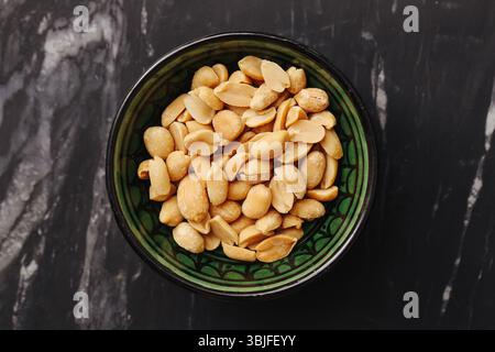 Salted peanuts in bowl. Golden roasted snack. Healthy vegan protein. Marble background flatlay. Organic crunchy texture. High energy food. Stock Photo