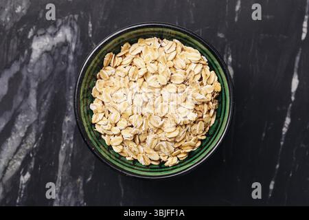 Oat flakes in bowl. Healthy breakfast idea. Dry cereal on dark marble. Organic whole grain oats. Nutritious morning meal. Simple clean ingredients. Stock Photo
