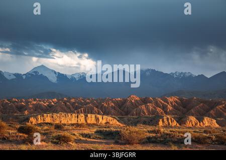The captivating sculpted red rock formations of Fairytale Canyon illuminated by the setting sun, with the snow-capped Tian Shan mountains in the backg Stock Photo