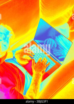Infrared Thermal image of man typing laptop on modern sofa. Ideal for remote work, home office, freelance, and digital lifestyle. Male hands typing on laptop Stock Photo