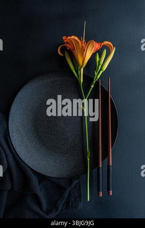 Overhead view of an Asian place setting with chopsticks and an orange tiger lily flower on a table Stock Photo