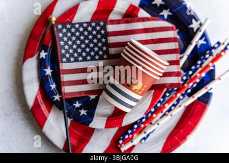 Overhead view of a stack of paper cups, paper plates, drinking straws and an american flag on a table for Independence Day on fourth of July Stock Photo
