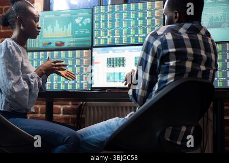 Focused male and female colleagues at desk, analyzing real time stock market charts on multiple monitors in a modern office. The tech savvy workspace includes trading software and data. Stock Photo