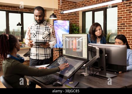 Multiethnic colleagues utilizing digital technology during their creative brainstorming session in modern workspace. Diverse team of employees working together in developing project designs in office. Stock Photo