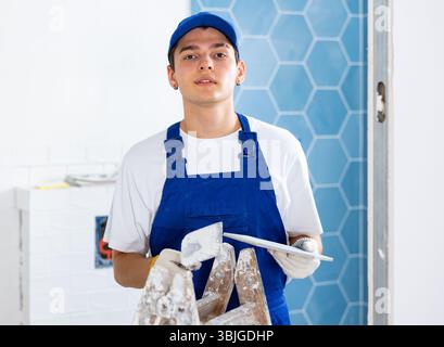 Construction worker in work clothes engaged in wall tiling work during overhauls indoors Stock Photo