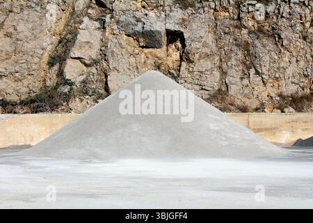 Large conical pile of fine gravel sits on a flat surface in a quarry, backed by a steep rocky wall, highlighting extraction and construction materials Stock Photo