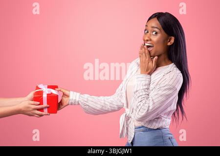 Surprised young lady receiving gift from female friend on pink studio background Stock Photo