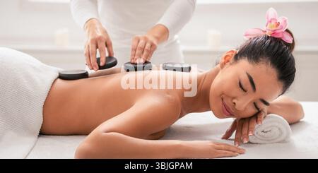 Relaxed asian woman enjoying hot stones back massage in spa salon Stock Photo