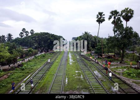 View of train tracks behind Jessore station, Bangladesh, with pedestrians walking along the rails through wet grass in the post-monsoon season. Stock Photo