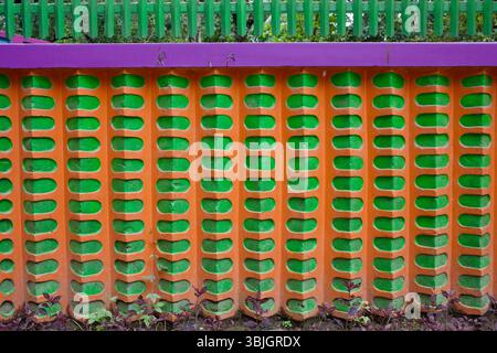 Detail of a brightly painted concrete wall with a repeating pattern in orange, green, and purple in Jessore, Bangladesh. Stock Photo