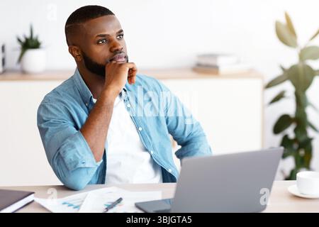 Black Freelancer Guy Sitting At Workplace With Thoughtful Face Expression Stock Photo