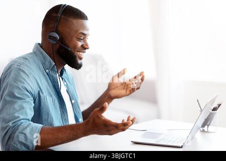 Web Conference. Friendly black guy in headset making video call on laptop Stock Photo
