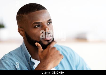 Portrait Of Thoughtful Black Millennial Man Touching Chin And Looking Away Stock Photo
