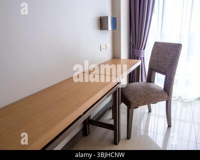 Empty luxury wooden chair with fabric pad and long wood table shelf at working area on white wall background near large glass window with curtains, in Stock Photo