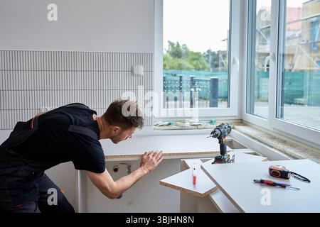 Worker aligns kitchen countertop panel in bright interior with tools. Professional furniture installation and home improvement process Stock Photo