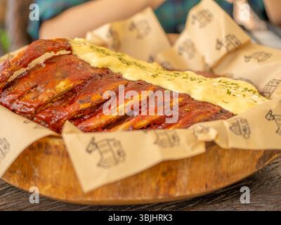 Delicious pork ribs with yellow mustard sauce served on plate cut into strips and wrapped in brown paper for restaurant menu presentation showcasing Stock Photo