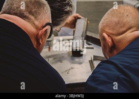 Worker examining a weld seam on a metal component using specialized equipment in a laboratory environment. Stock Photo