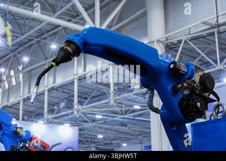 A blue robot arm with a welding torch in a manufacturing facility under bright lighting. Stock Photo