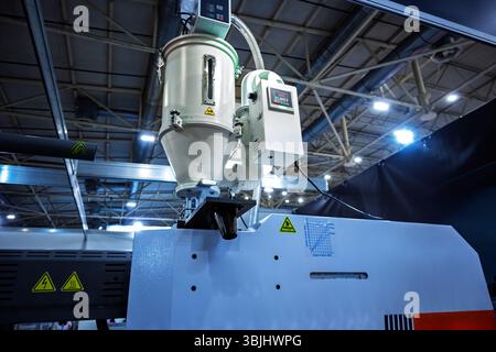 Close-up view of industrial plastic processing machinery in a factory setting, showing hopper, control unit, warning symbols, and technical details Stock Photo