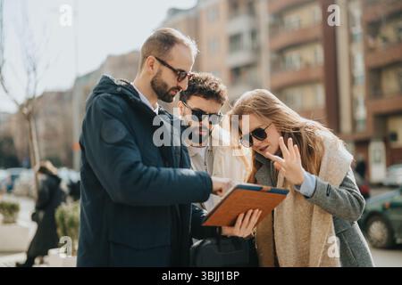 Three people discussing something on a tablet outdoors in an urban area Stock Photo
