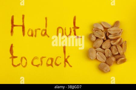 Caramelized peanuts on a yellow background with the words hard nuts to crack Stock Photo