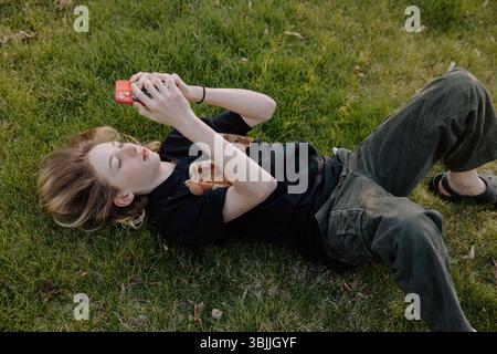 Teenager boy lying on grass using smartphone outdoors Stock Photo