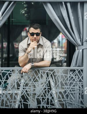 man in a light shirt and sunglasses leans against a decorative railing Stock Photo
