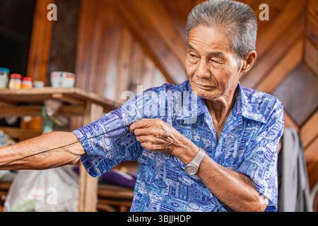 Elderly man stretches rope for broom crafting Stock Photo