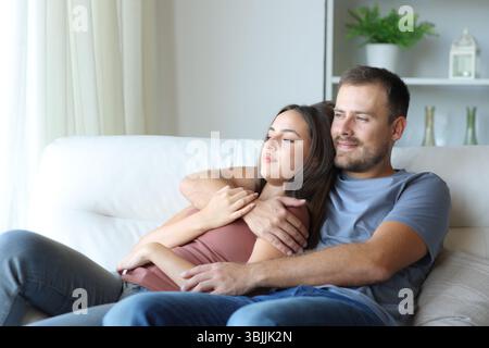 Relaxed couple looking away sitting on a couch at home Stock Photo