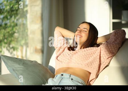Happy woman relaxing sitting on a sofa at sunset sitting on a couch at home Stock Photo