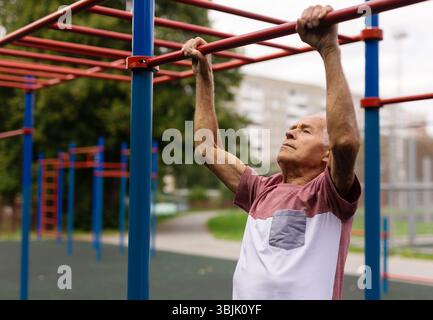 Sportive old man doing pull-ups outdoors Stock Photo