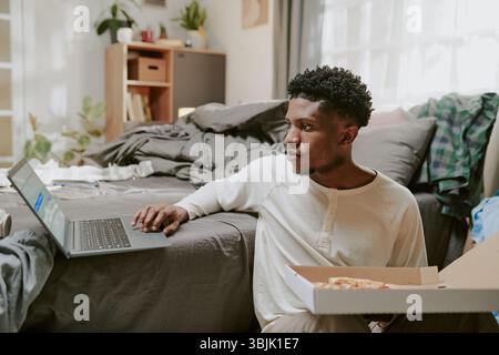 Young Man Using Laptop While Sitting on Bed Stock Photo