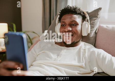 Smiling Man Listening to Music on Headphones While Holding Phone Stock Photo
