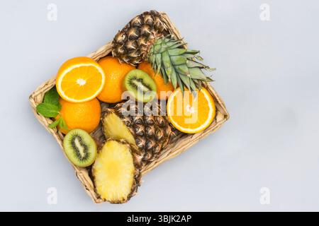 Pineapple, orange and kiwi sliced in rattan basket. . Gray background. Flat lay Stock Photo