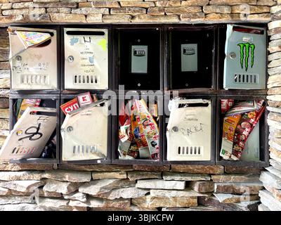 Outdoor postboxes mounted on stone wall of residential building, with some broken units and several key lockboxes for self check-in short-term rentals Stock Photo