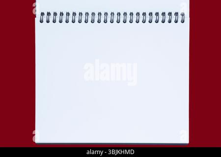 close up of  blank white page of opened sketchbook with spiral binder against red background Stock Photo