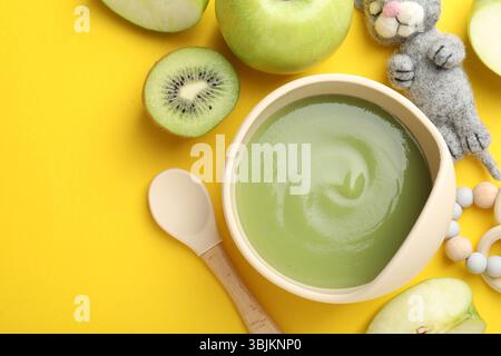 Baby food. Tasty puree in bowls, different ingredients and toys on yellow background, flat lay. Space for text Stock Photo