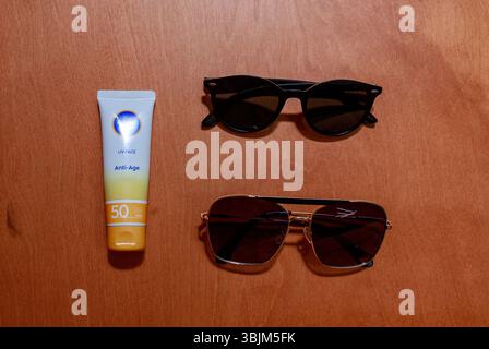 Flatlay of sunscreen and two pairs of sunglasses arranged on wooden background. Stock Photo